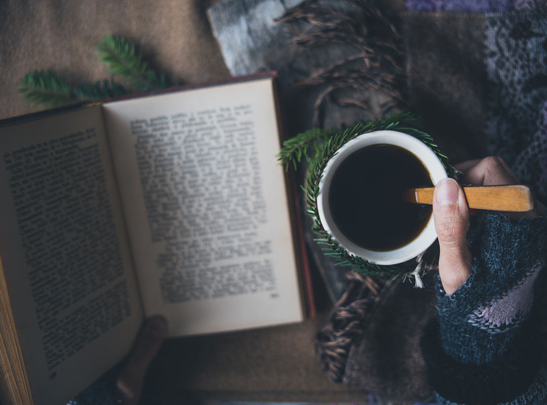 A woman reading a book open on hr lap, with a mug of coffee.