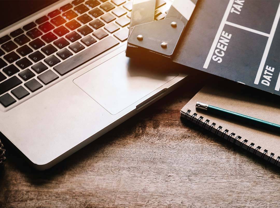 A laptop on a desk with a note pad, pen and film clapper.